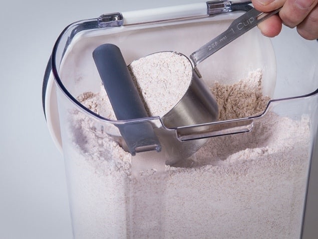 Progressive Flour keeper + with view of magnetic, removable leveler leveling off a cup of flour inside the keeper