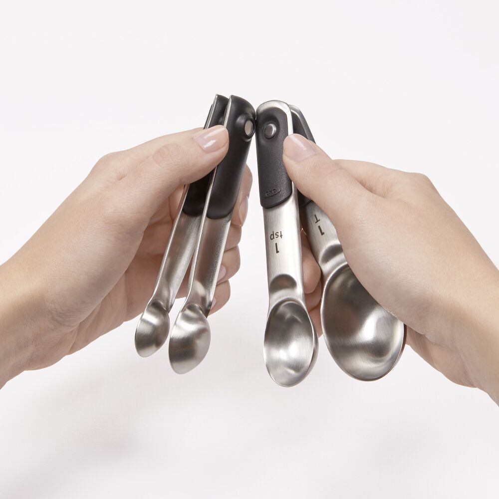 Two hands holding a set of metal measuring spoons against a white background