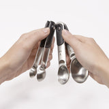Two hands holding a set of metal measuring spoons against a white background