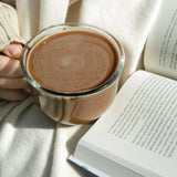 A cup of Bare Life Dairy Free & Vegan Hot Cocoa with a book
