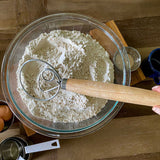 Glass bowl with flour and a Danish whisk on a wooden surface