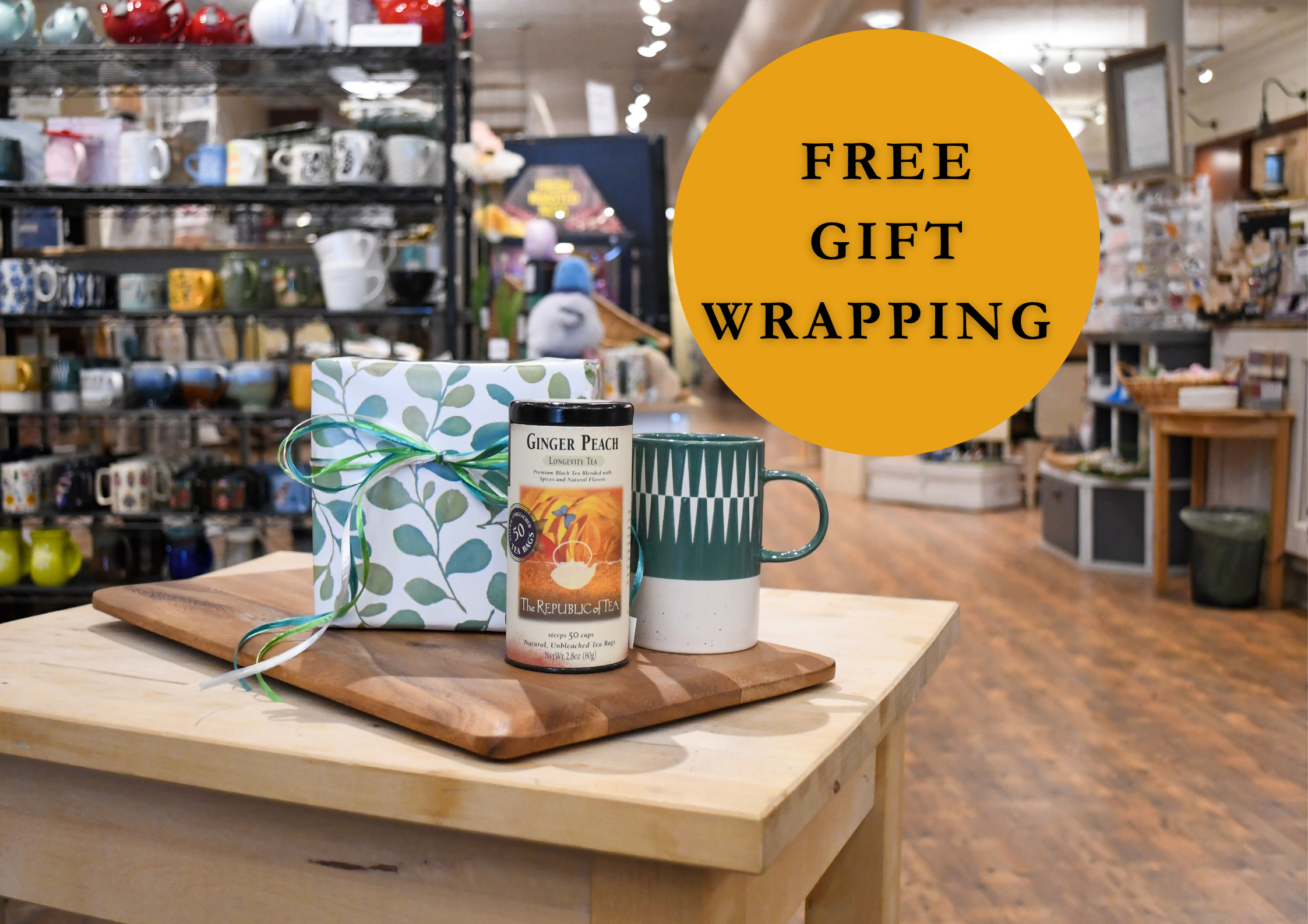 Table with a mug, gift box, and bottle of ginger ale with 'Free Gift Wrapping' text in a store setting.