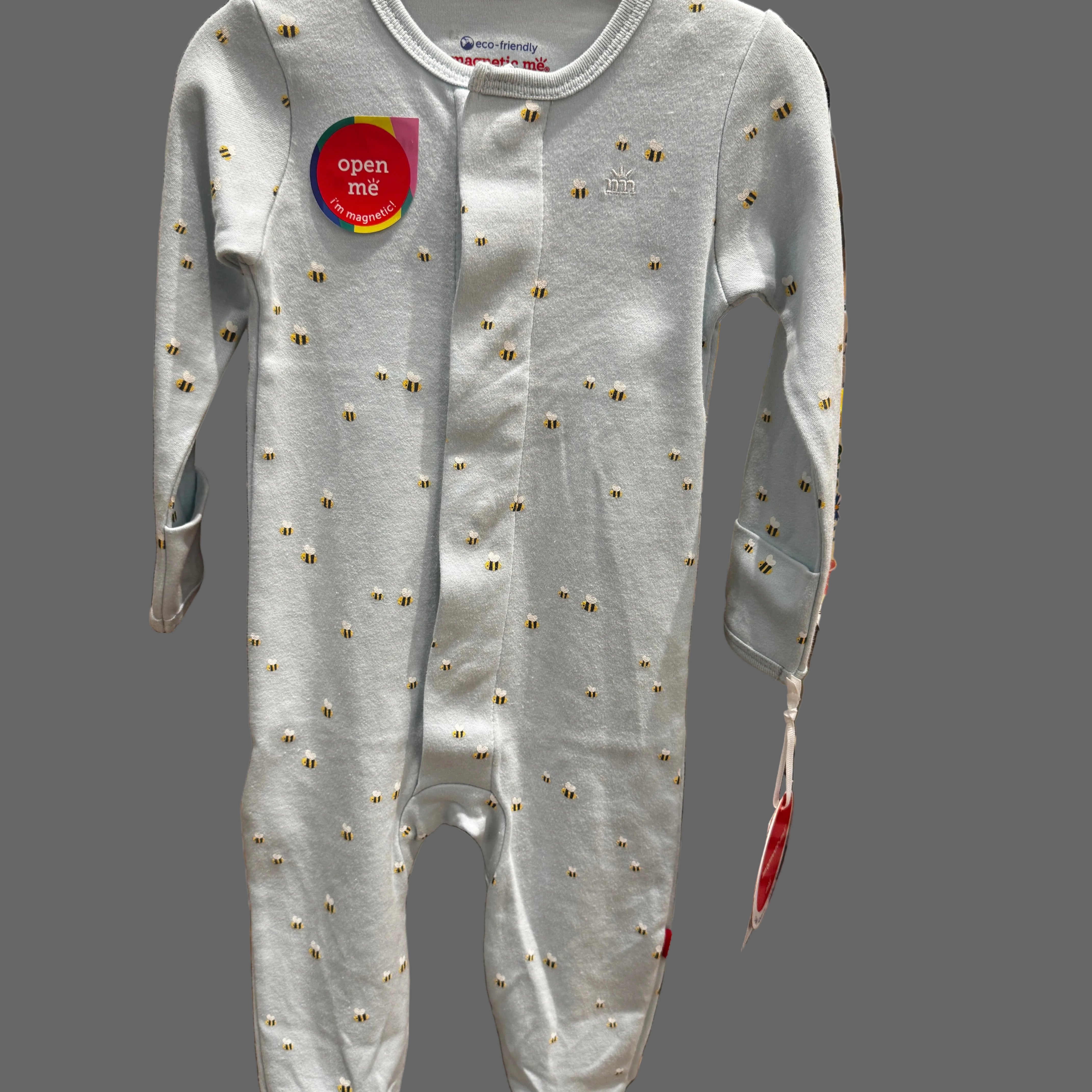 A baby long-sleeve footed sleeper in light gray with small gold embroidered details, shown hanging on a store display.