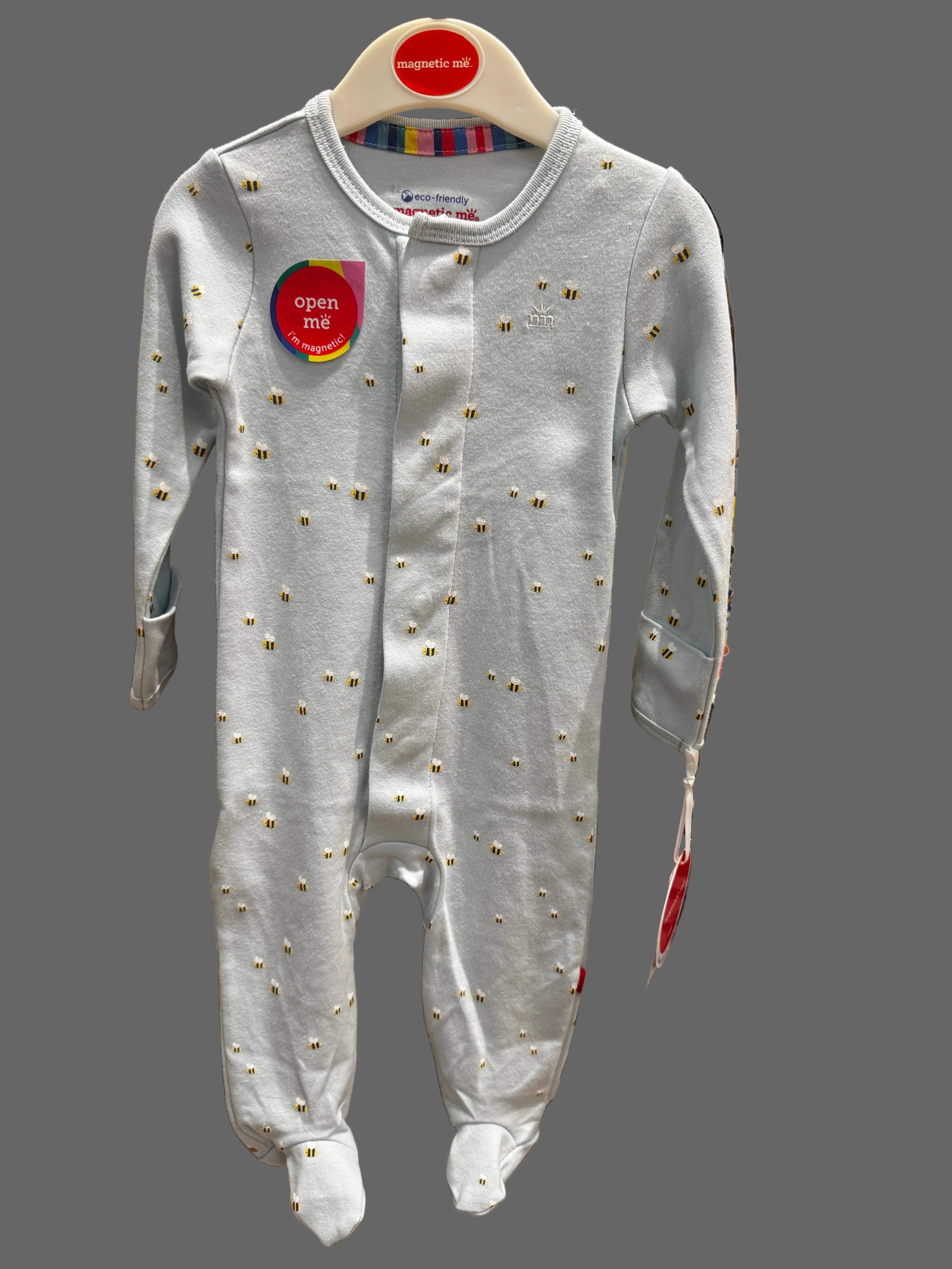 A baby long-sleeve footed sleeper in light gray with small gold embroidered details, shown hanging on a store display.