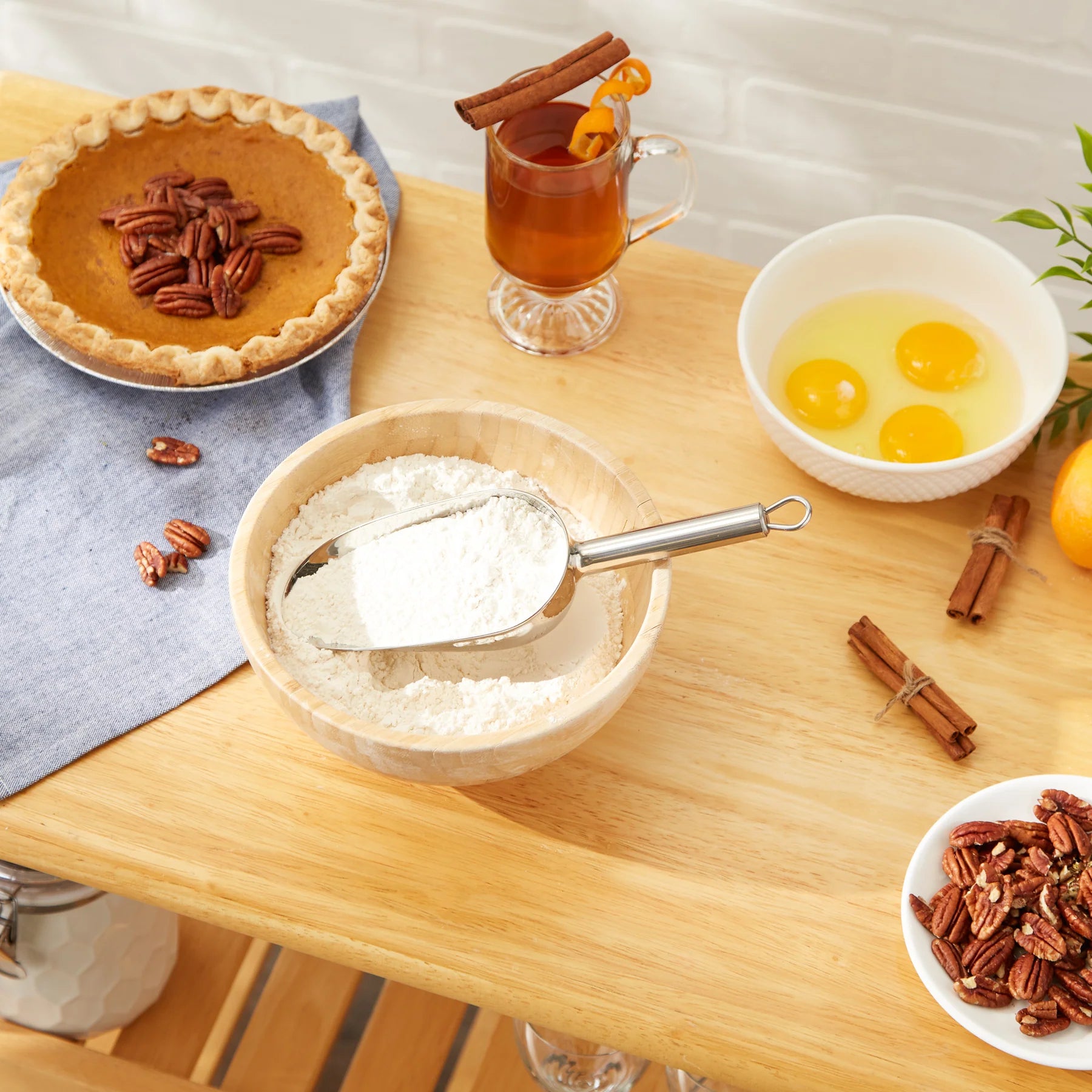 Scene with RSVP scoop in bowl of flour, baking ingredients and a pecan pie