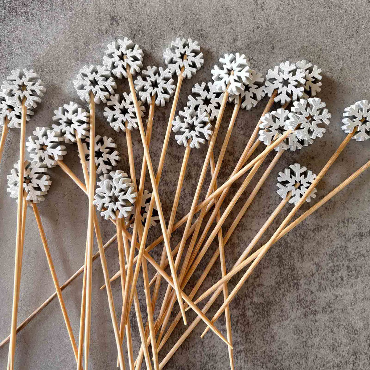 White snowflake decorations on wooden sticks against a gray background