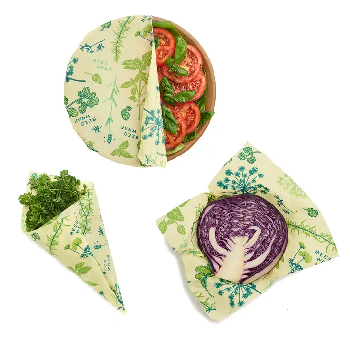 Bees Wrap Assorted 3 Pack (S, M, L) Herb Garden wrapping herbs, a salad in a bowl, and a half of cabbage.