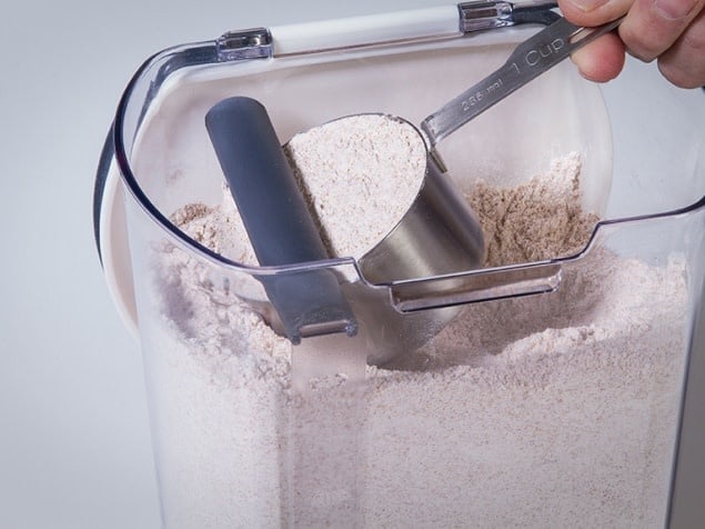 Progressive Flour keeper + with view of  magnetic, removable leveler  leveling off a cup of flour inside the keeper