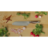 Chef's knife on a wooden cutting board with vegetables and herbs