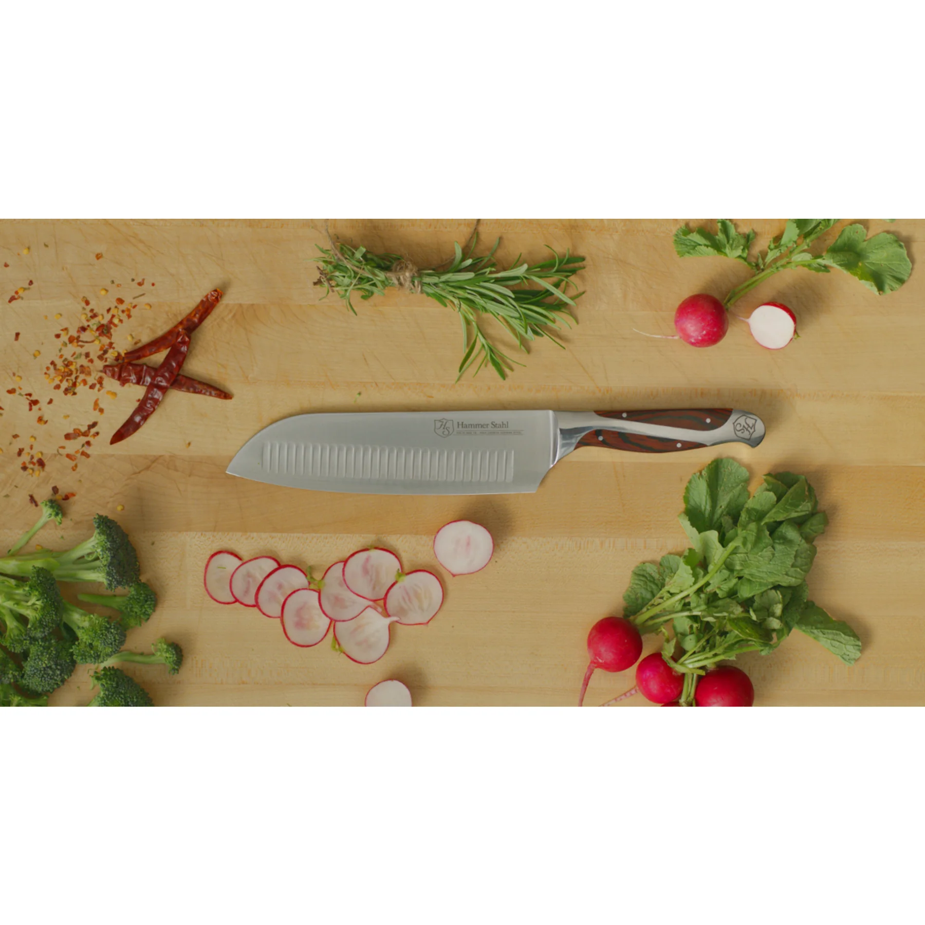 Chef's knife on a wooden cutting board with vegetables and herbs