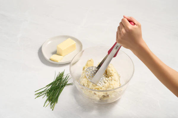 The Zyliss Stainless Steel Potato Masher mashing a potato with butter and chives